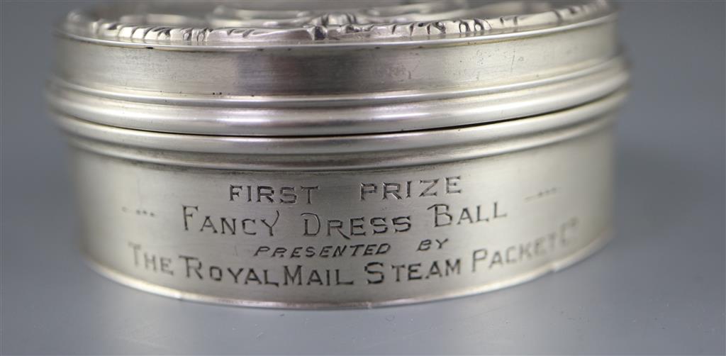 A George V silver circular box and hinged cover, embossed with a ship and dancing figures above,